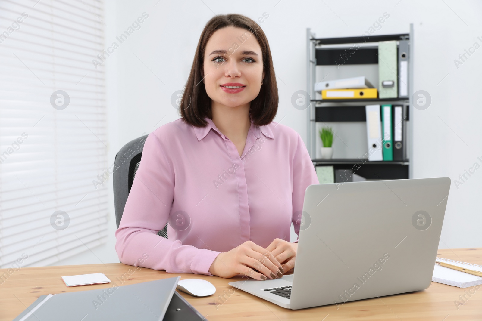 Photo of Happy young intern working with laptop at table in modern office