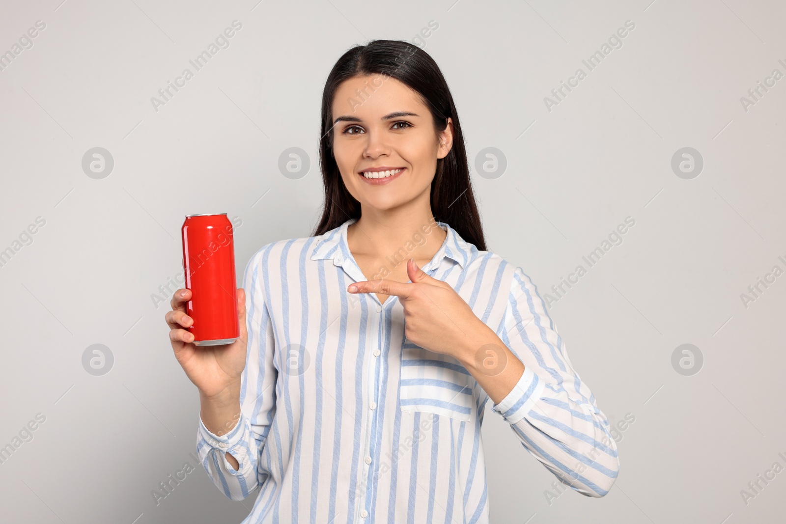 Photo of Beautiful young woman holding tin can with beverage on light grey background