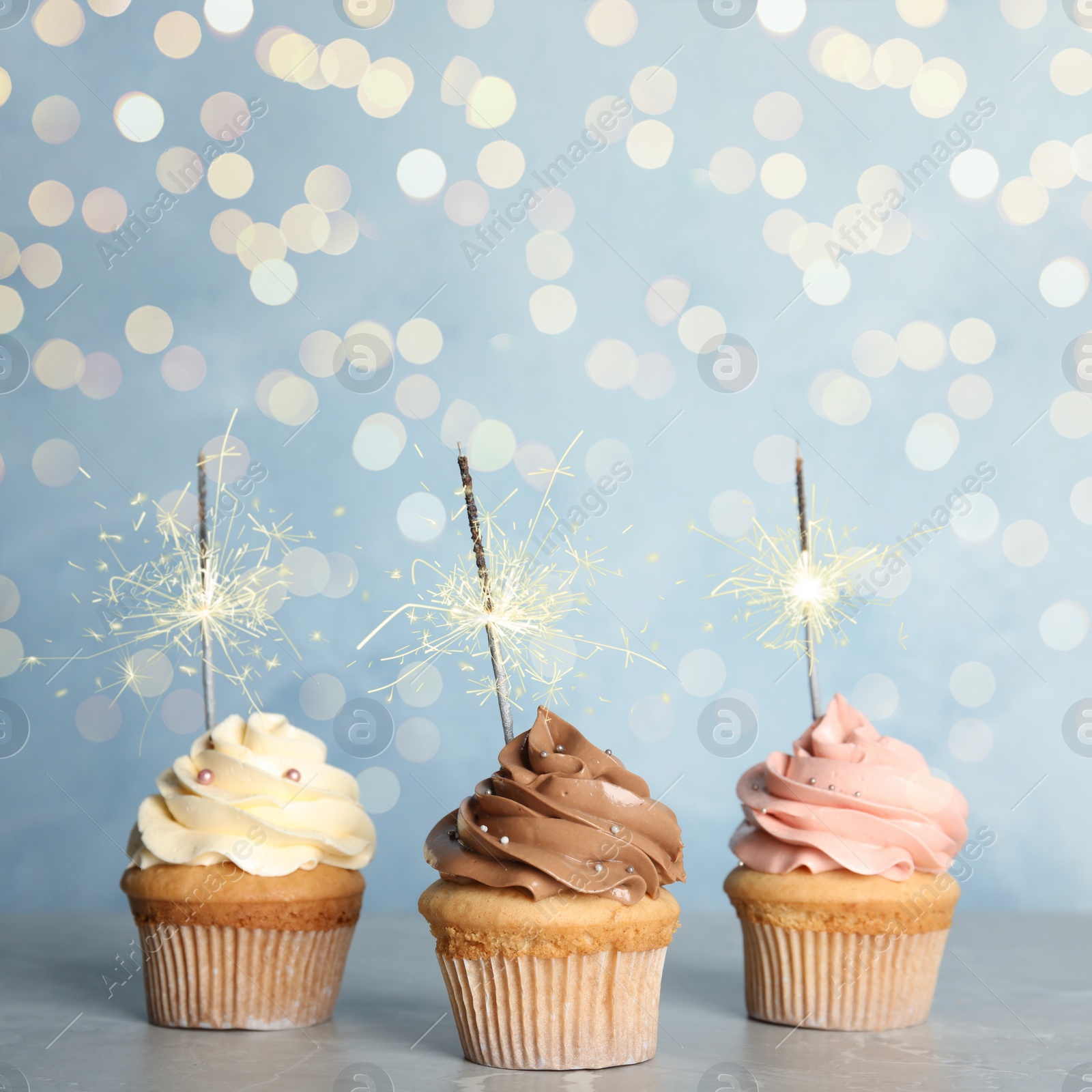 Image of Birthday cupcakes with sparklers on table against light blue background