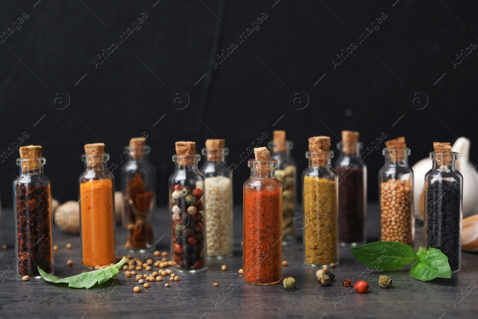 Photo of Glass bottles with different spices on table against black background