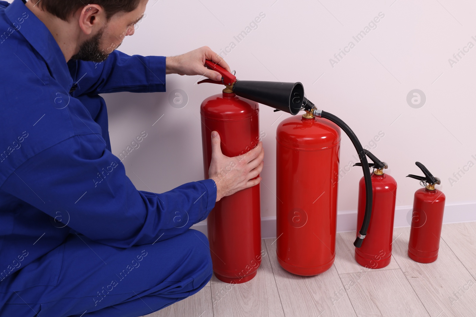 Photo of Man checking quality of fire extinguishers indoors, closeup