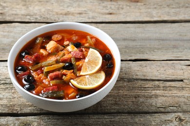 Meat solyanka soup with sausages, olives and vegetables in bowl on wooden table. Space for text