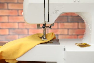 Photo of Sewing machine with yellow fabric on table indoors, closeup