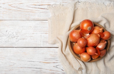 Photo of Bowl with fresh ripe onions on wooden table, top view