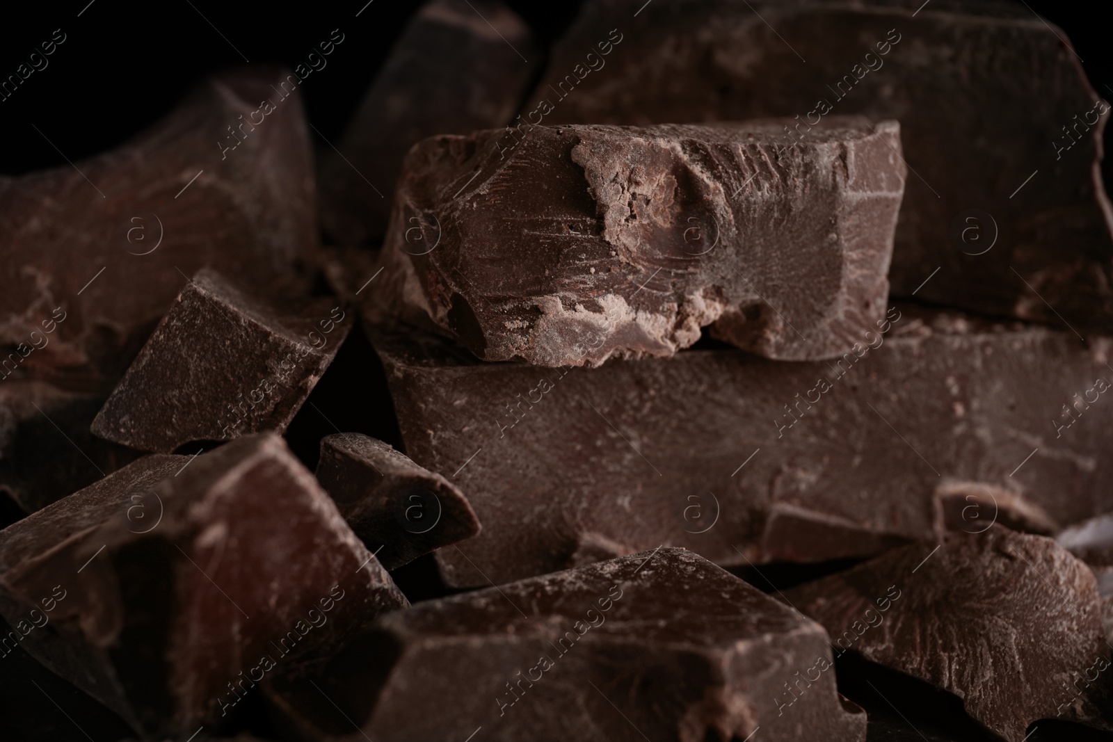 Photo of Pieces of tasty dark chocolate on black background, closeup