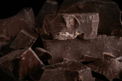Photo of Pieces of tasty dark chocolate on black background, closeup