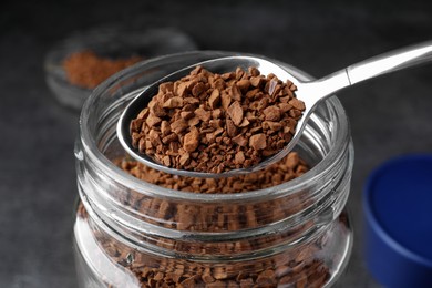 Instant coffee and spoon above glass jar on table, closeup