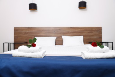 Clean folded towels with flowers on bed in hotel room