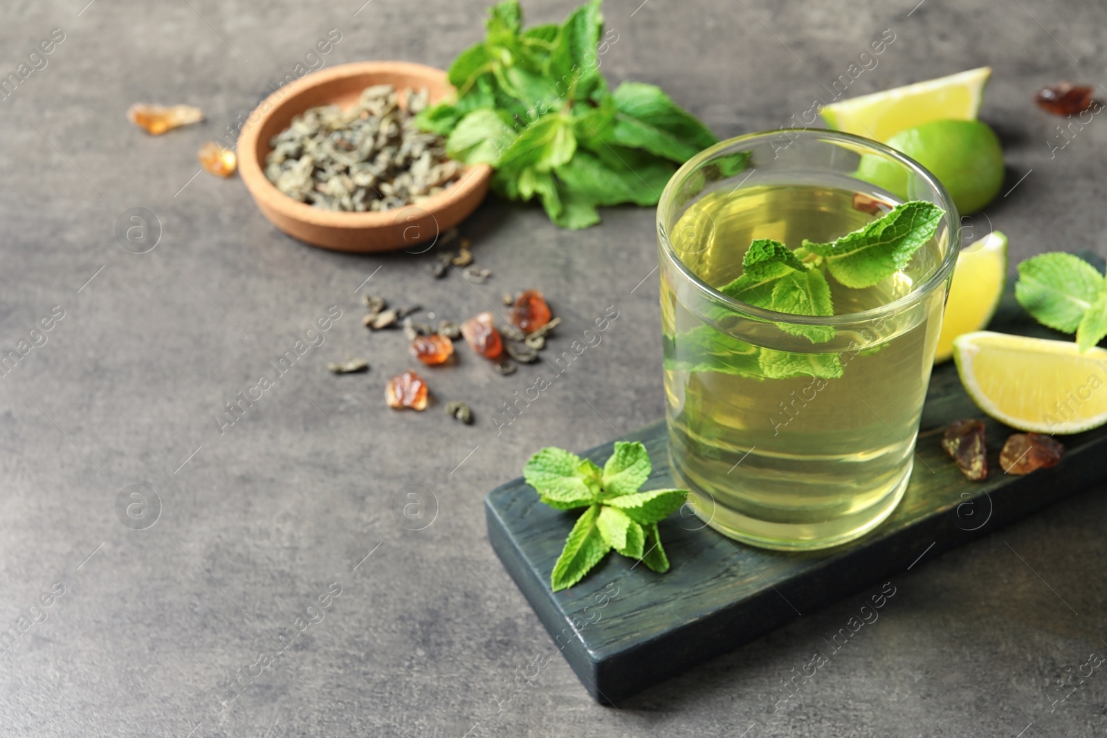 Photo of Glass with hot aromatic mint tea, fresh leaves and lime on table