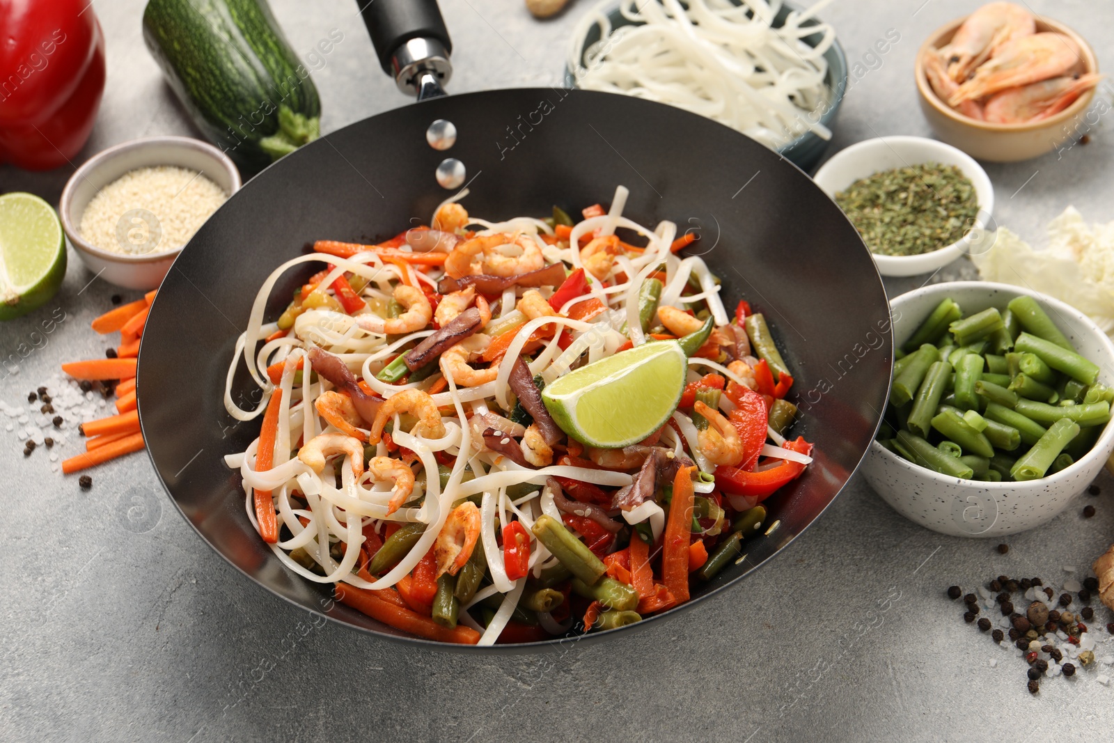 Photo of Shrimp stir fry with noodles and vegetables in wok on grey table