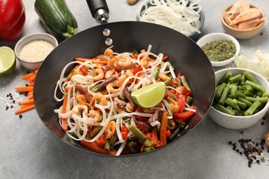 Shrimp stir fry with noodles and vegetables in wok on grey table