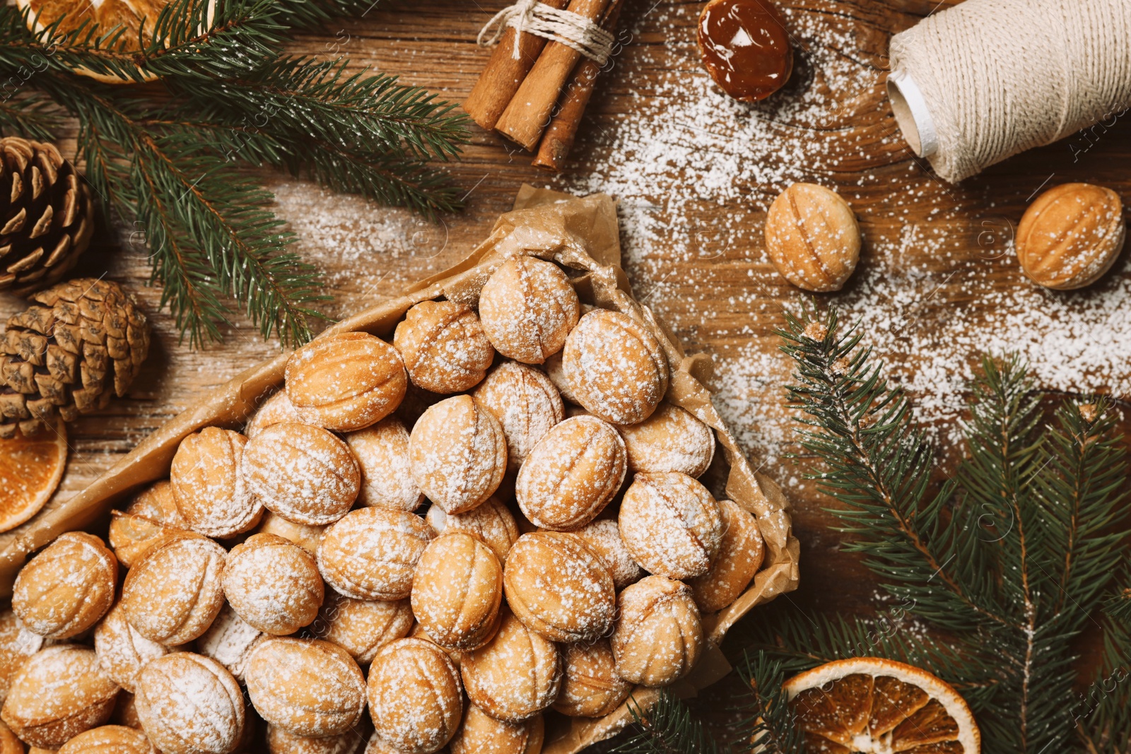 Photo of Delicious nut shaped cookies with boiled condensed milk, dry orange slices and fir tree branches on wooden table, flat lay