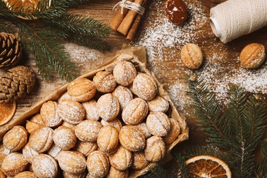 Delicious nut shaped cookies with boiled condensed milk, dry orange slices and fir tree branches on wooden table, flat lay