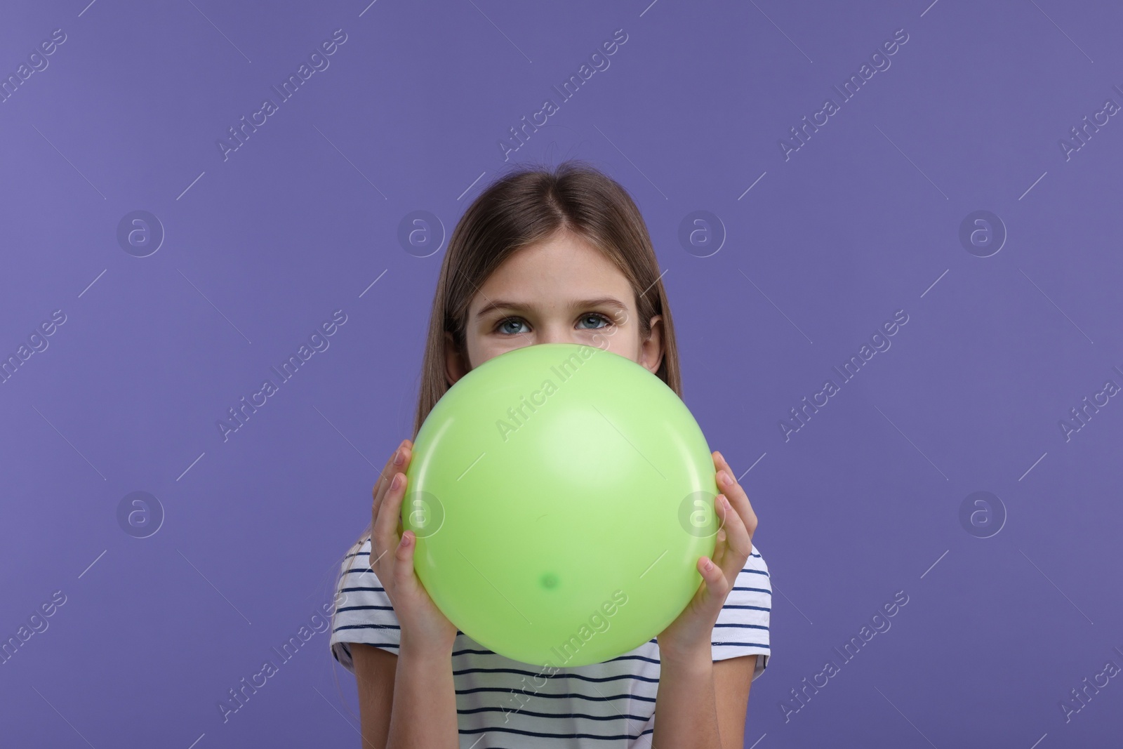 Photo of Girl inflating light green balloon on violet background