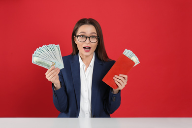 Photo of Emotional young woman with money and wallet at table on crimson background