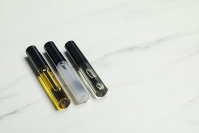 Photo of Tubes of different eyelash oils on white marble table. Space for text