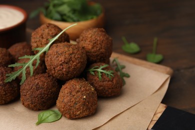 Photo of Delicious falafel balls, arugula and basil on wooden table, space for text