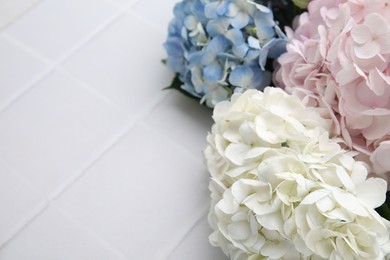 Photo of Beautiful hydrangea flowers on white tiled background, closeup. Space for text