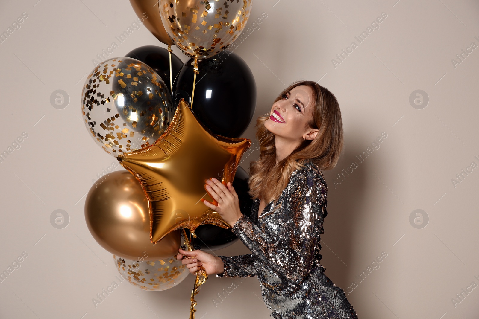 Photo of Happy woman in silver shiny dress with air balloons on beige background. Christmas party