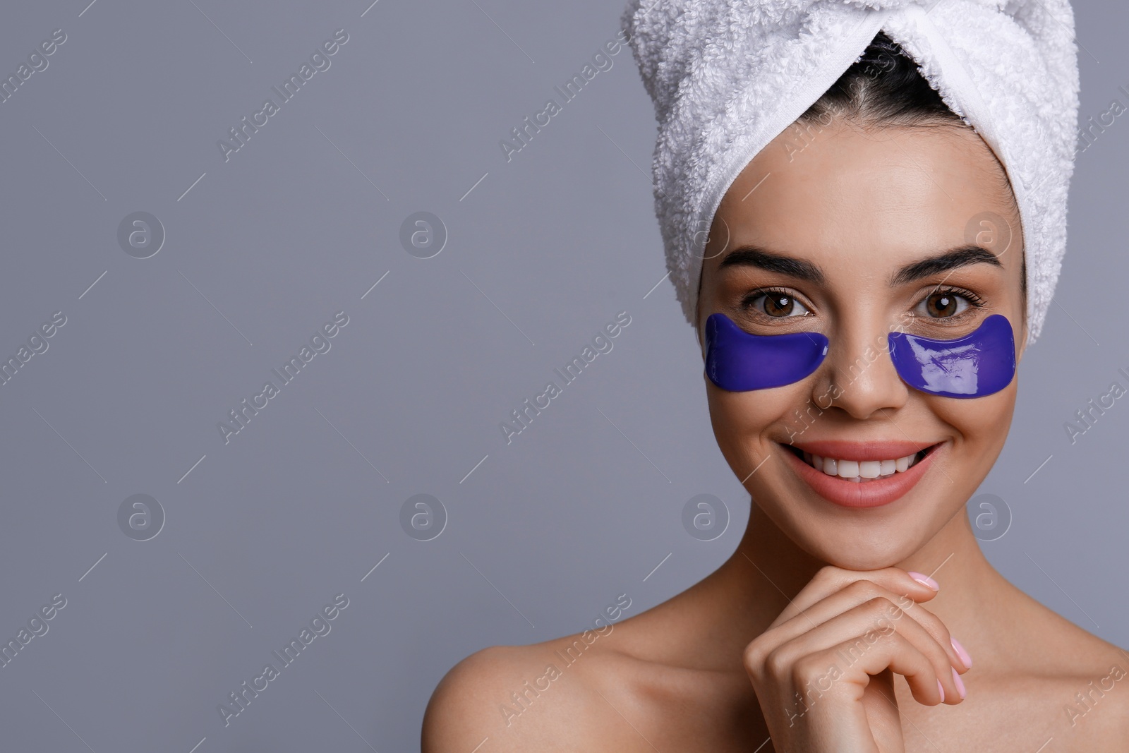 Photo of Beautiful young woman with under eye patches and hair wrapped in towel on grey background, space for text