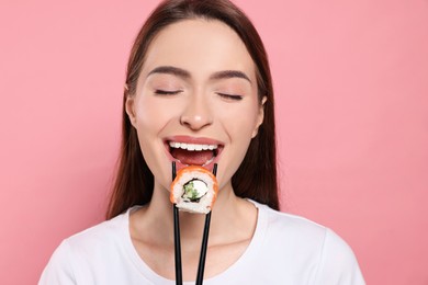 Photo of Beautiful young woman eating sushi roll with chopsticks on pink background