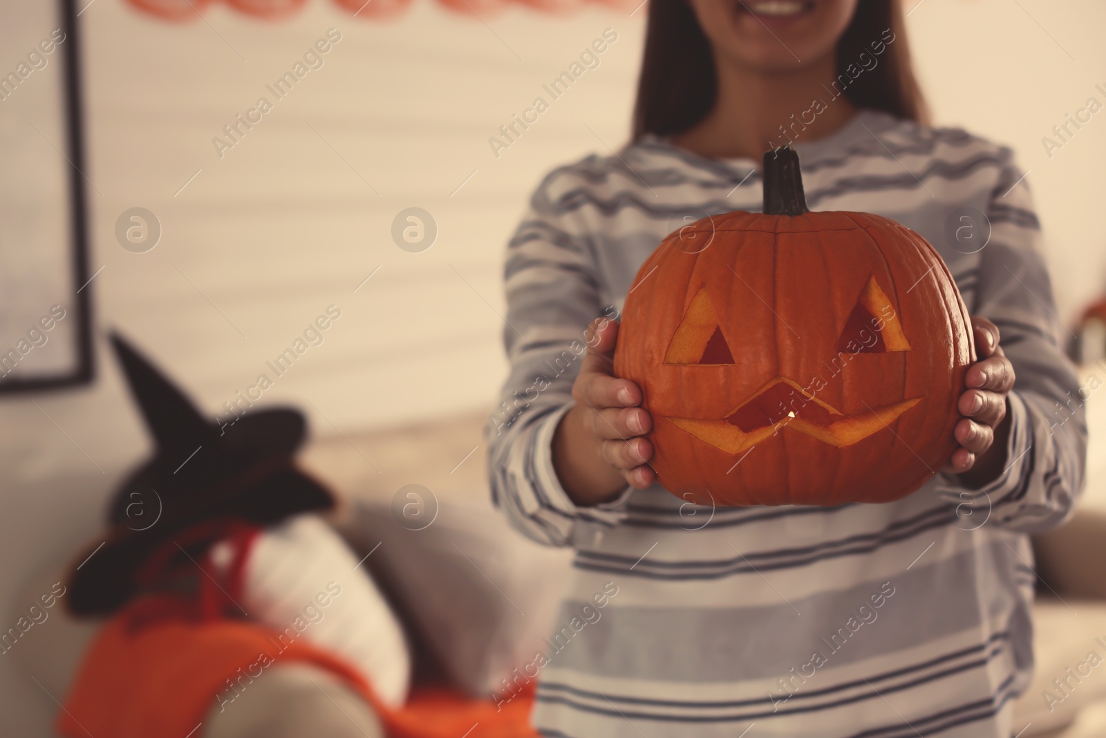 Photo of Woman holding pumpkin jack o'lantern indoors, closeup with space for text. Halloween celebration