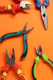 Different pliers on orange background, flat lay