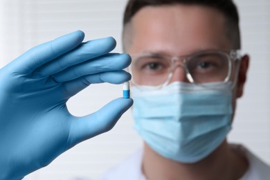 Doctor holding pill on light background, selective focus. Space for text