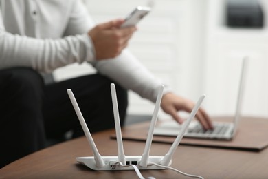 Photo of Man with smartphone and laptop working at wooden table, focus on Wi-Fi router