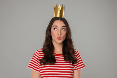 Beautiful young woman with princess crown sending air kiss on grey background