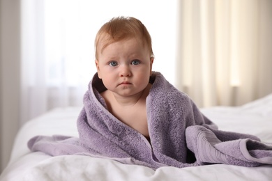 Photo of Cute little baby with soft purple towel on bed after bath