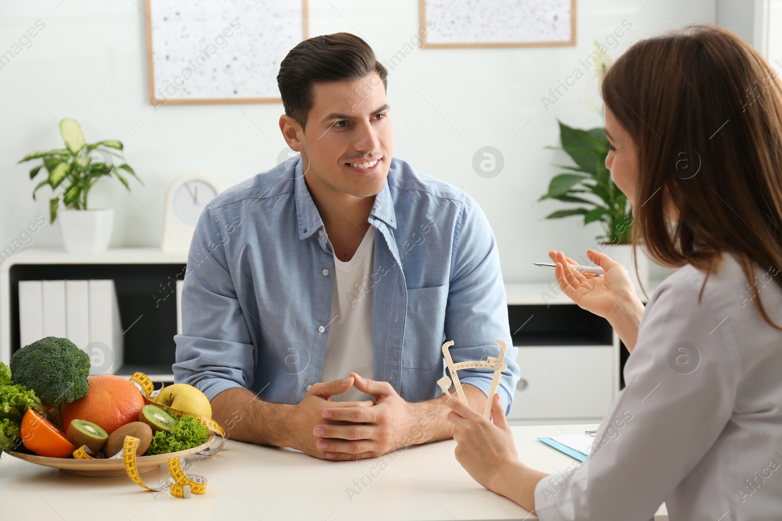 Photo of Young nutritionist consulting patient at table in clinic