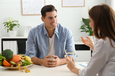 Photo of Young nutritionist consulting patient at table in clinic