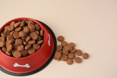 Photo of Dry dog food and feeding bowl on beige background. Space for text