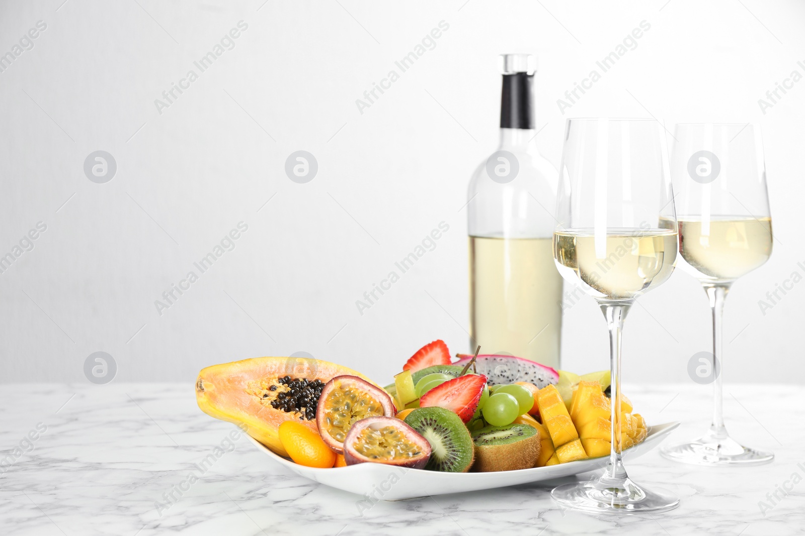 Photo of Delicious exotic fruits and wine on white marble table. Space for text