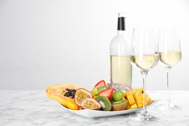 Photo of Delicious exotic fruits and wine on white marble table. Space for text