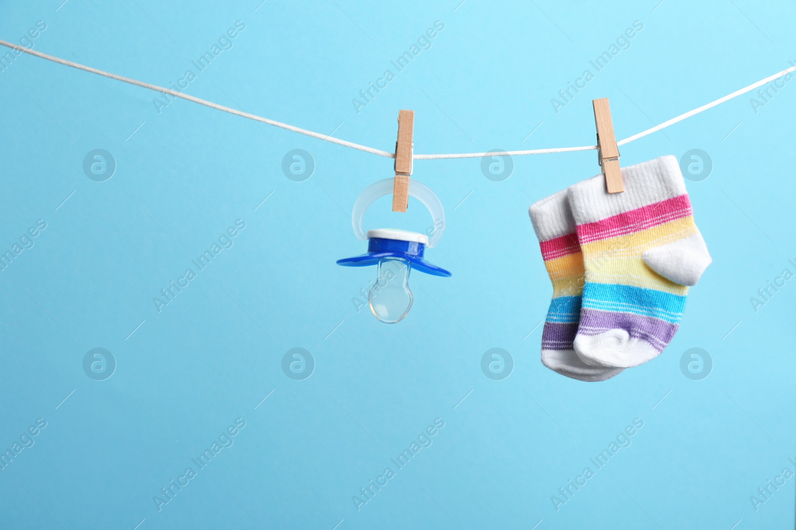 Photo of Small socks and pacifier hanging on washing line against color background, space for text. Baby accessories