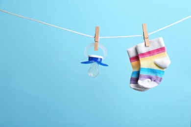 Photo of Small socks and pacifier hanging on washing line against color background, space for text. Baby accessories