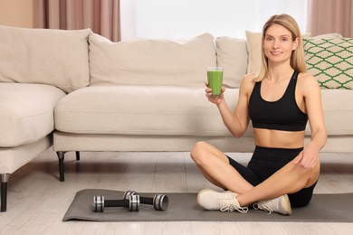 Photo of Young woman in sportswear with glass of fresh smoothie at home