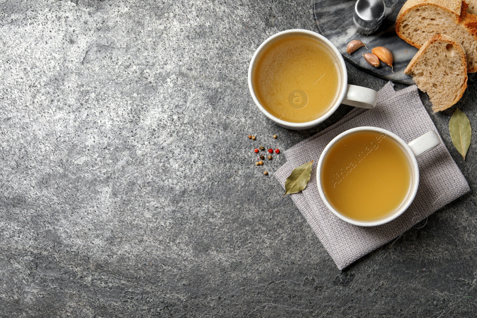 Photo of Hot delicious bouillon in cups on grey table, flat lay. Space for text