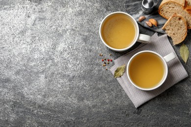 Hot delicious bouillon in cups on grey table, flat lay. Space for text