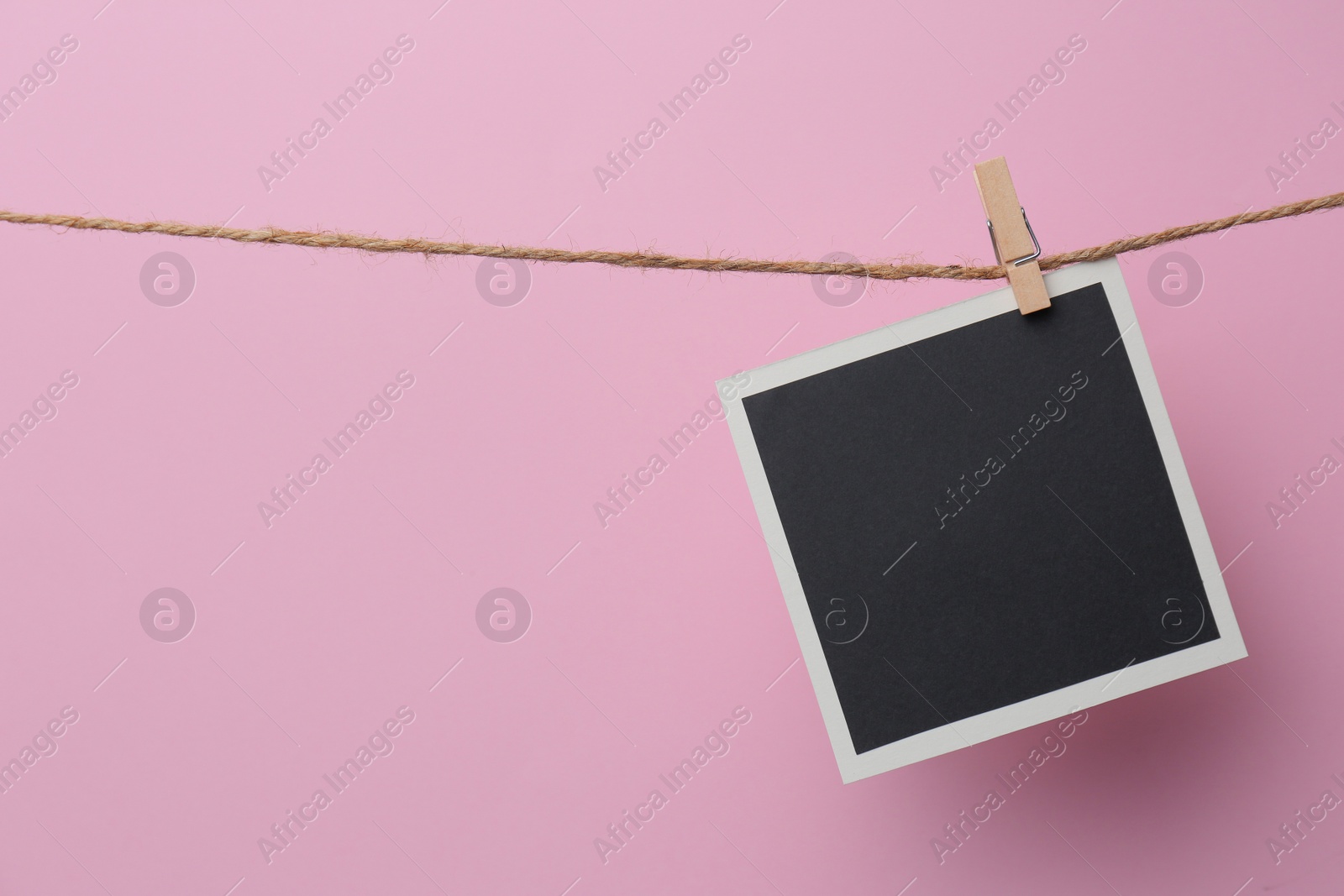 Photo of Wooden clothespin with empty instant frame on twine against pink background. Space for text