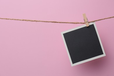 Photo of Wooden clothespin with empty instant frame on twine against pink background. Space for text
