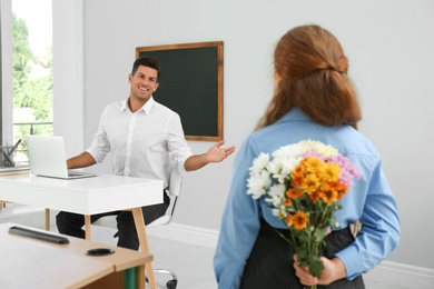 Photo of Schoolgirl with bouquet congratulating her pedagogue in classroom. Teacher's day