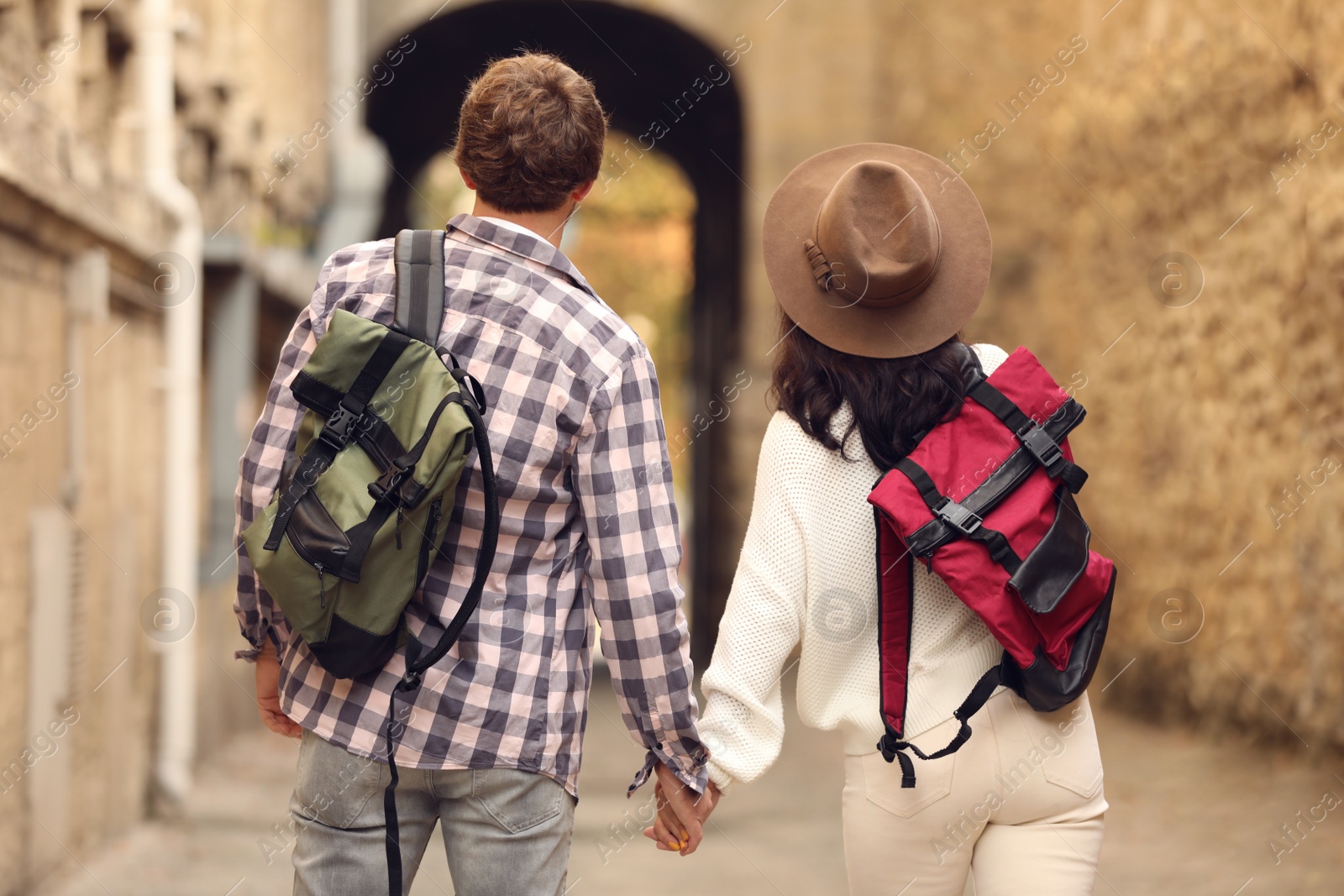 Photo of Couple of travelers with backpacks on city street, back view