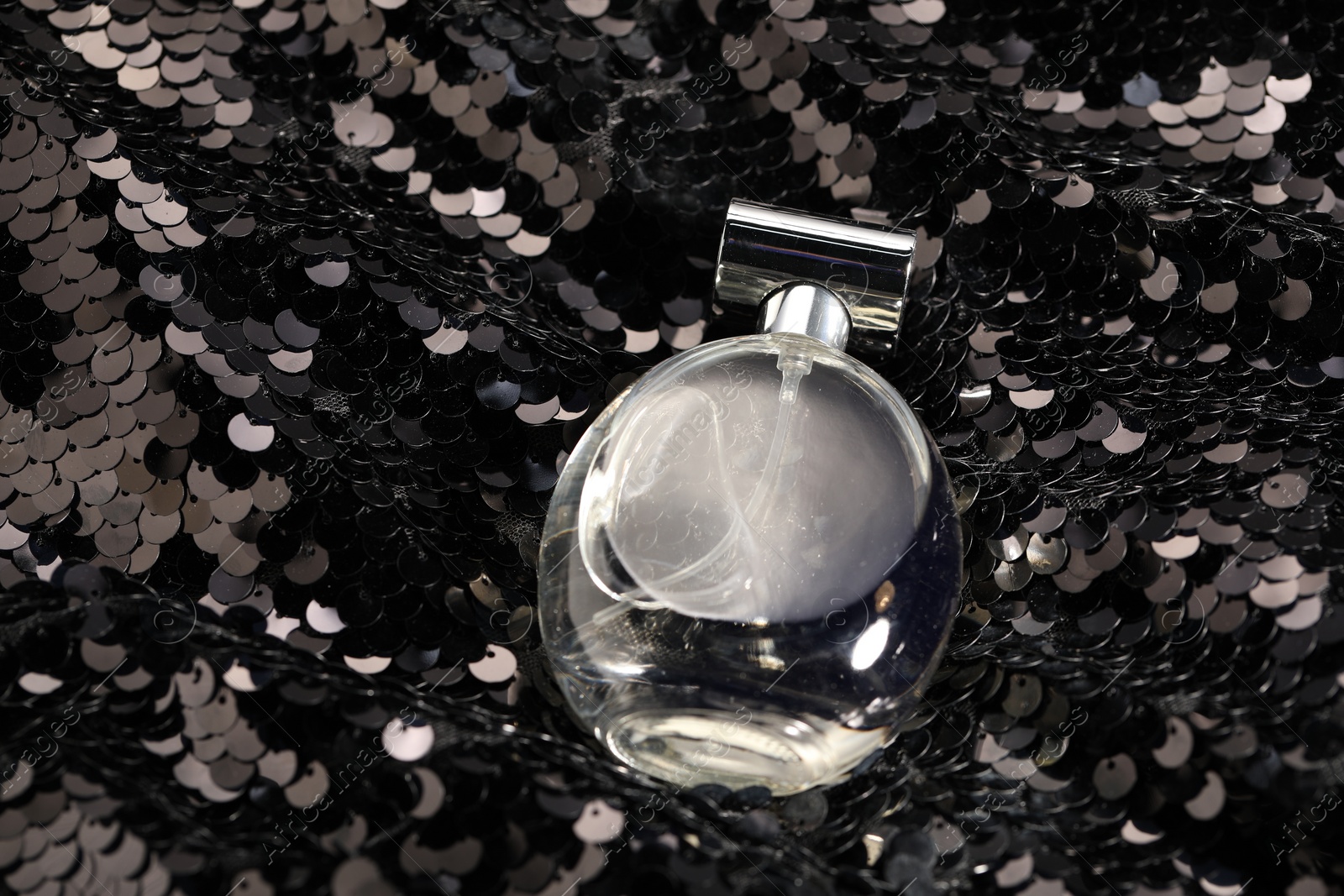 Photo of Luxury perfume in bottle on fabric with shiny sequins