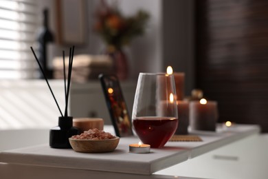 Photo of White wooden tray with glass of wine, beauty products and burning candle on bathtub in bathroom