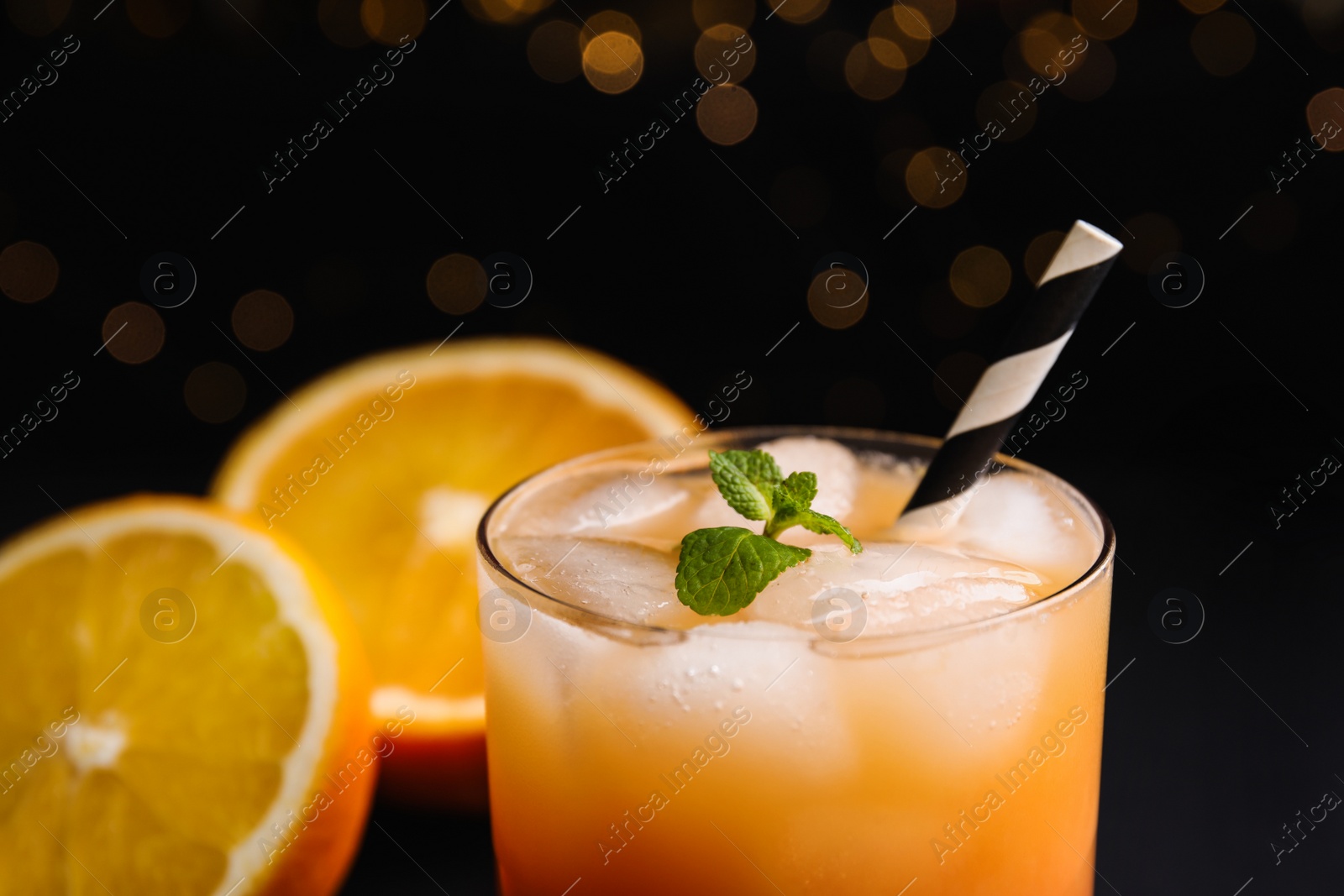 Photo of Fresh alcoholic Tequila Sunrise cocktail against blurred lights, closeup
