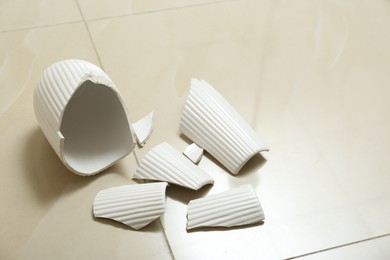 Photo of Broken white ceramic vase on floor indoors