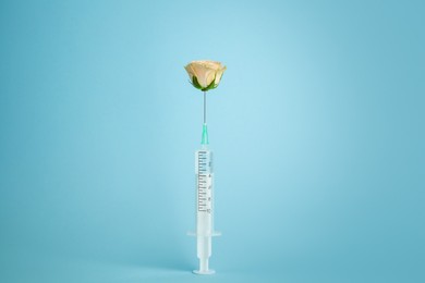 Photo of Medical syringe and beautiful rose on light blue background